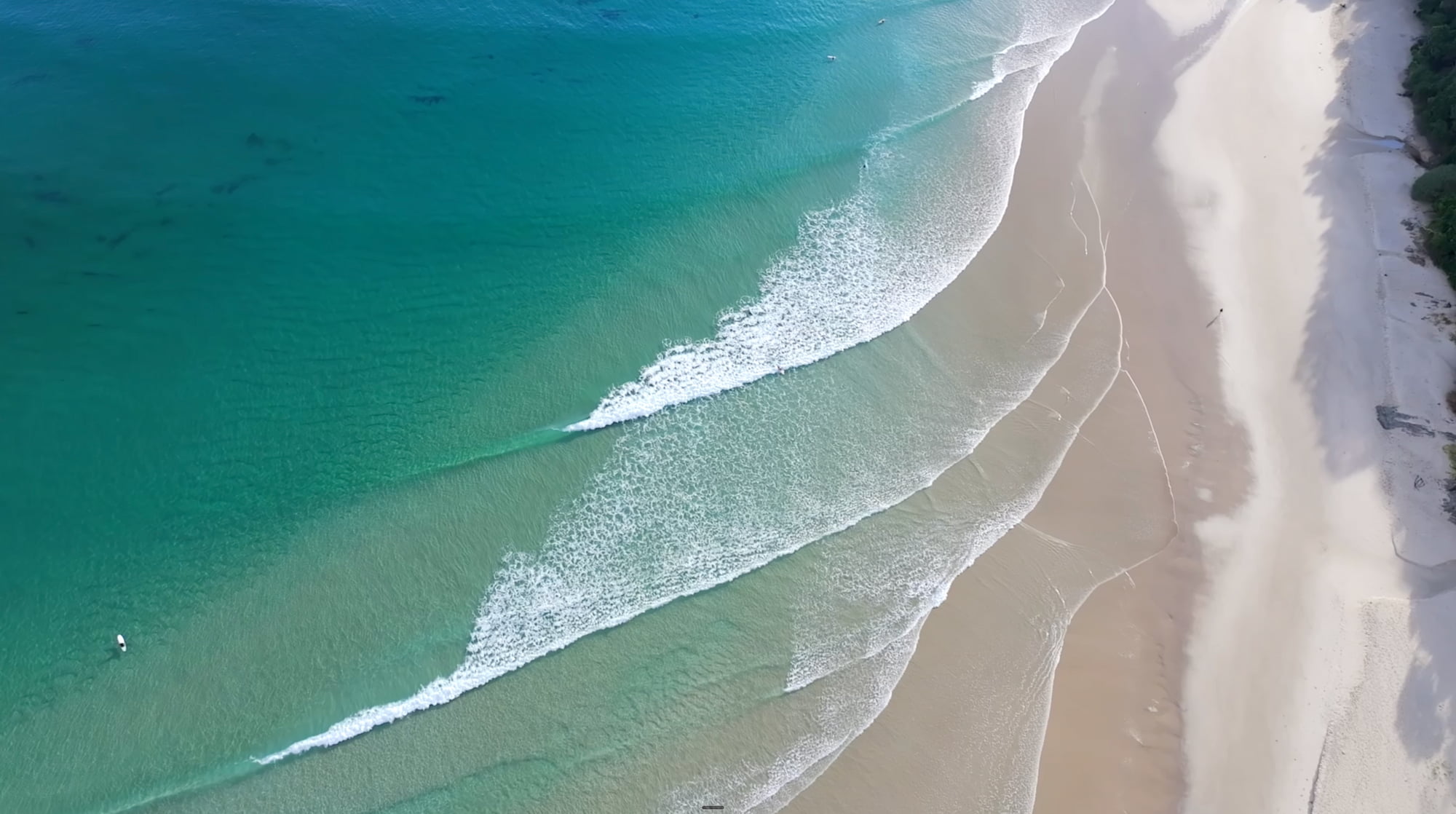 Aerial view of a Sunshine Coast beach, with surf breaking on white sand